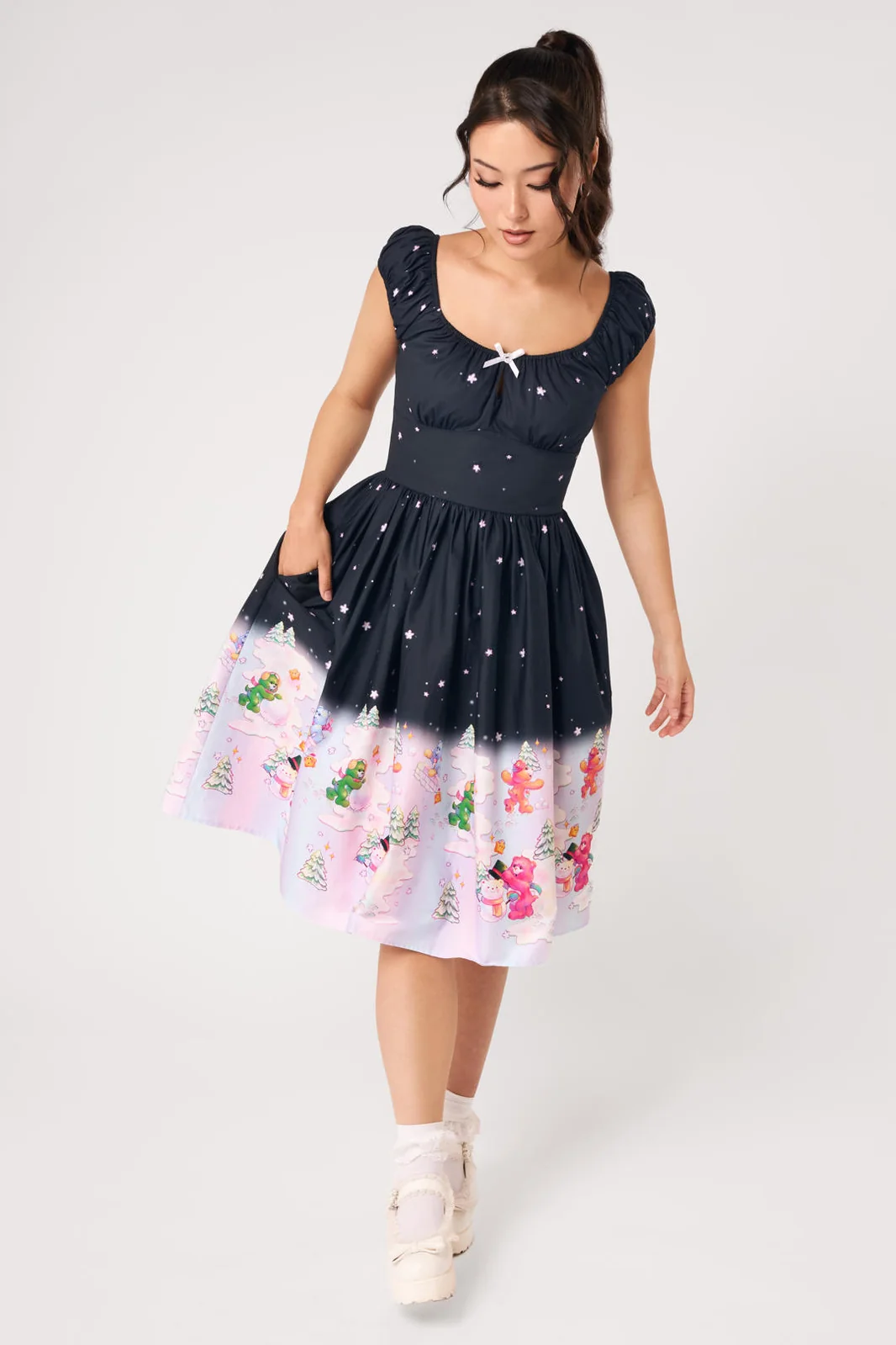 A woman modeling a sleeveless midi dress with a dark navy upper section and a pastel pink lower section featuring a floral print, set against a plain light gray studio background.