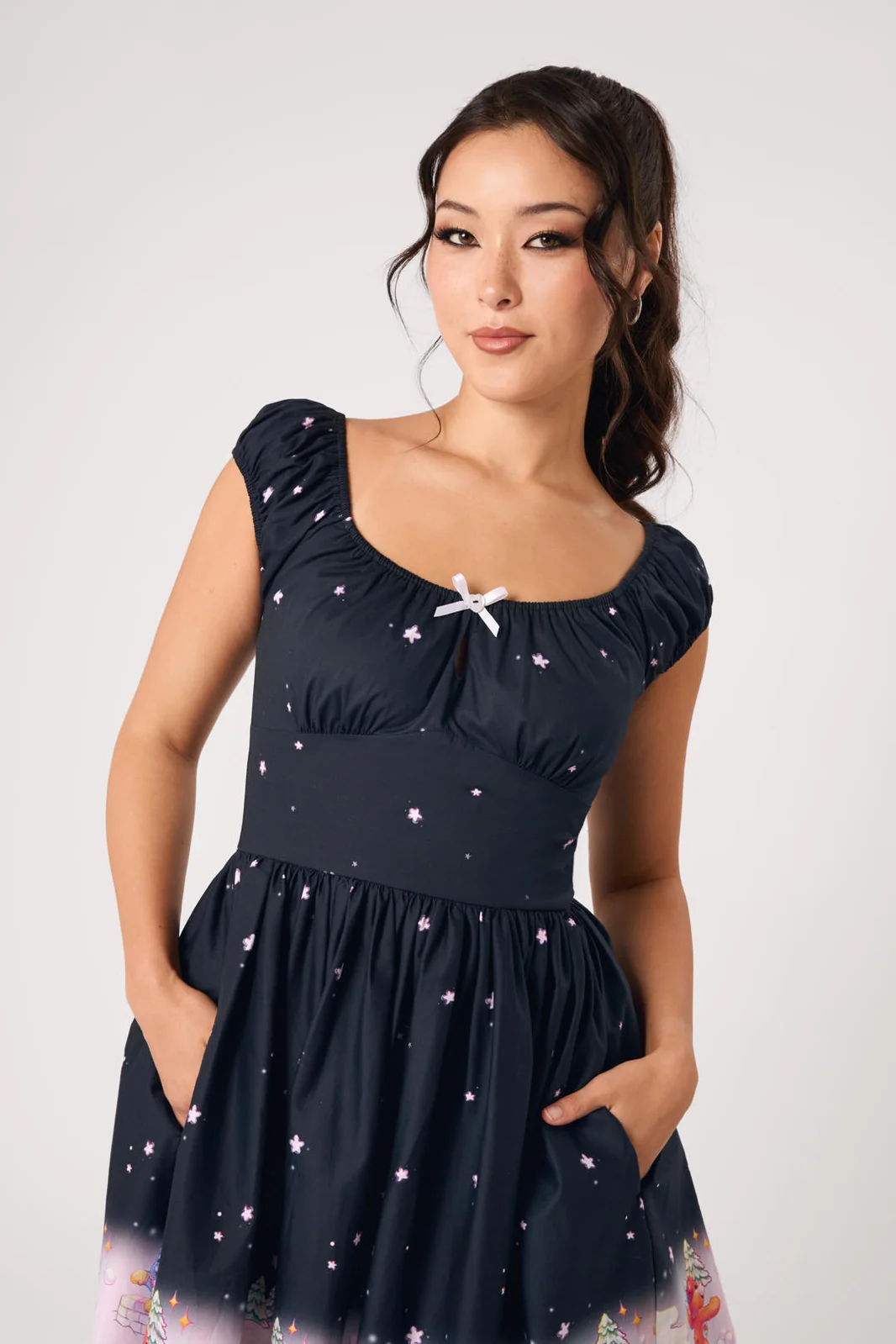 A woman modeling a navy blue swing dress with a starry pattern, featuring a sweetheart neckline with a white bow accent and pockets.