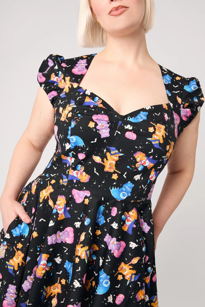 A woman wearing a black dress with a colorful retro cartoon character print, featuring puff sleeves and a sweetheart neckline, shown against a light gray background.