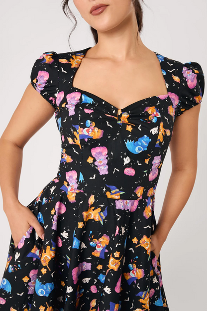 A woman wearing a black dress with a colorful cartoon character print, featuring puff sleeves, a sweetheart neckline, and a gathered waist.