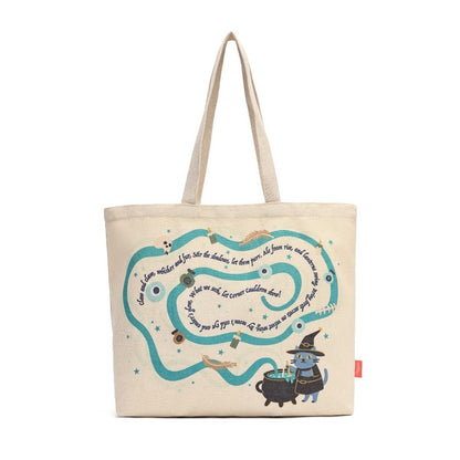 A beige canvas tote bag featuring a whimsical illustrated design with a winding teal path, small decorative objects, and a blue cat wearing a witch hat next to a cauldron. The bag has two beige shoulder straps and a small red tag on the right side, shown against a plain white background.