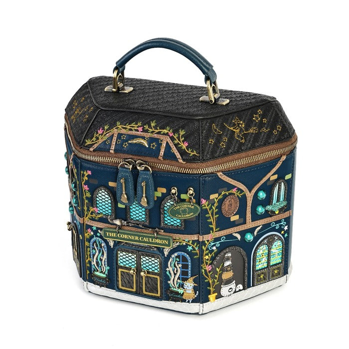 A hexagonal handbag designed to look like a whimsical building facade, featuring a dark navy blue base with intricate gold, green, and turquoise architectural illustrations, a black quilted top lid, and a dark blue handle.