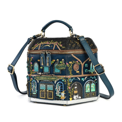 A dark blue handbag designed to look like a whimsical building facade, featuring gold zippers, a top handle, and a detachable shoulder strap. The front is decorated with colorful illustrations of characters and architectural details, including a sign reading 'THE CORNER CAUTION'.