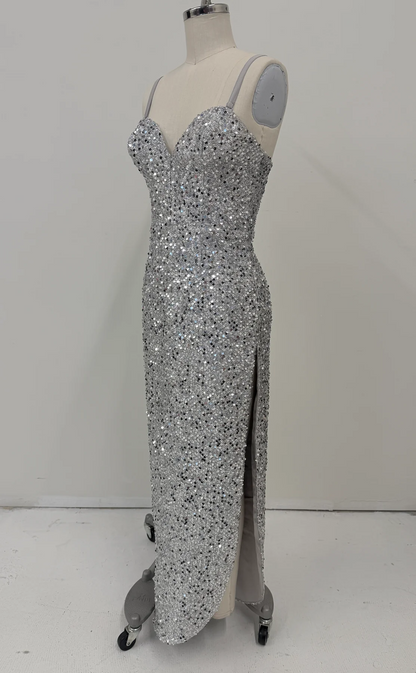 A floor-length silver sequin gown displayed on a mannequin with a high slit, photographed against a plain light gray wall and floor.