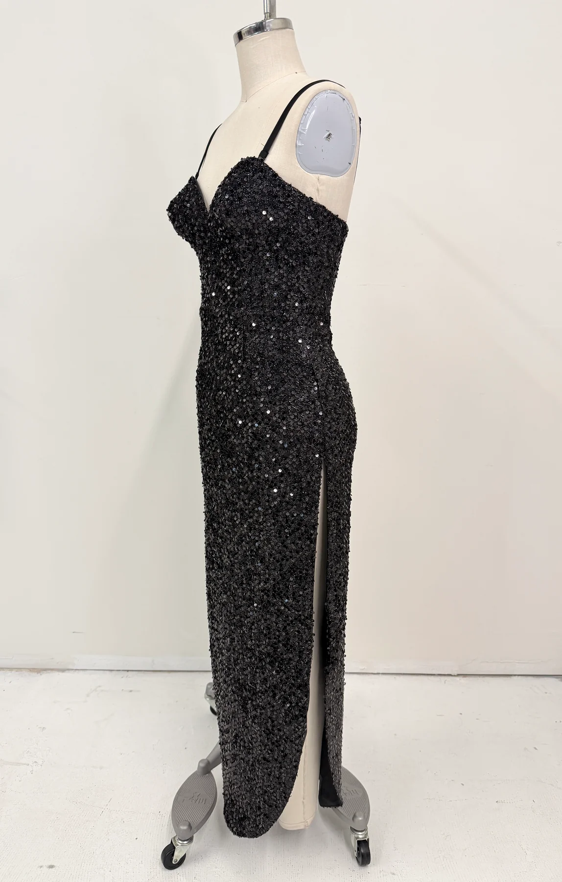 A black sequined evening gown with spaghetti straps and a thigh-high slit, displayed on a dress form mannequin against a plain off-white background.