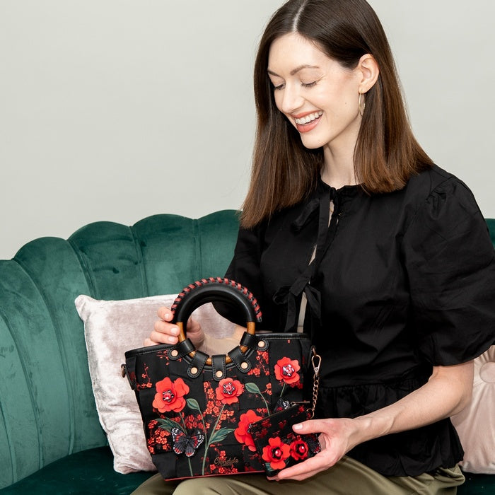 Woman holding a black handbag with red floral patterns on a green couch.