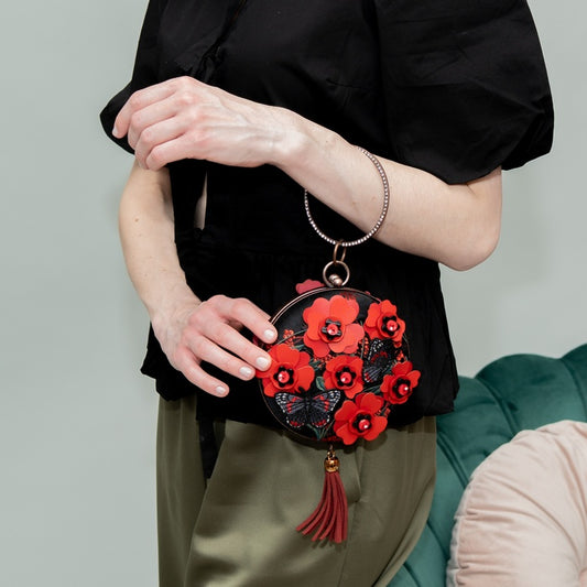 Person holding a black handbag with red floral designs against a neutral background