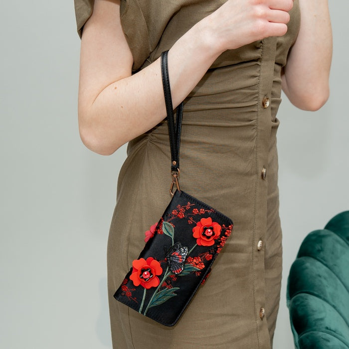 Person wearing a brown dress holding a black clutch with red floral designs.