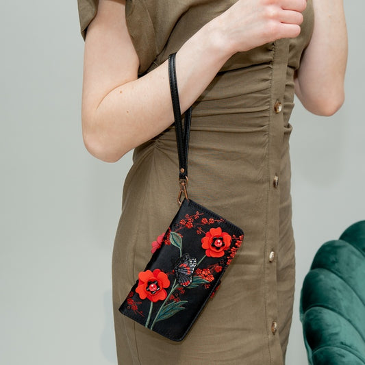 Person wearing a brown dress holding a black clutch with red floral designs.