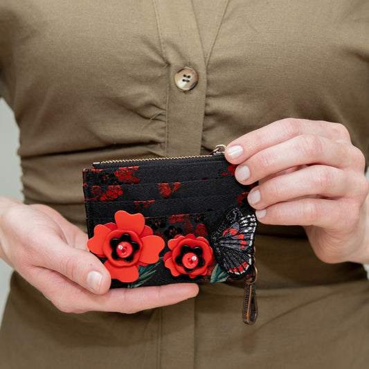 Person holding a black wallet with red floral and butterfly designs.