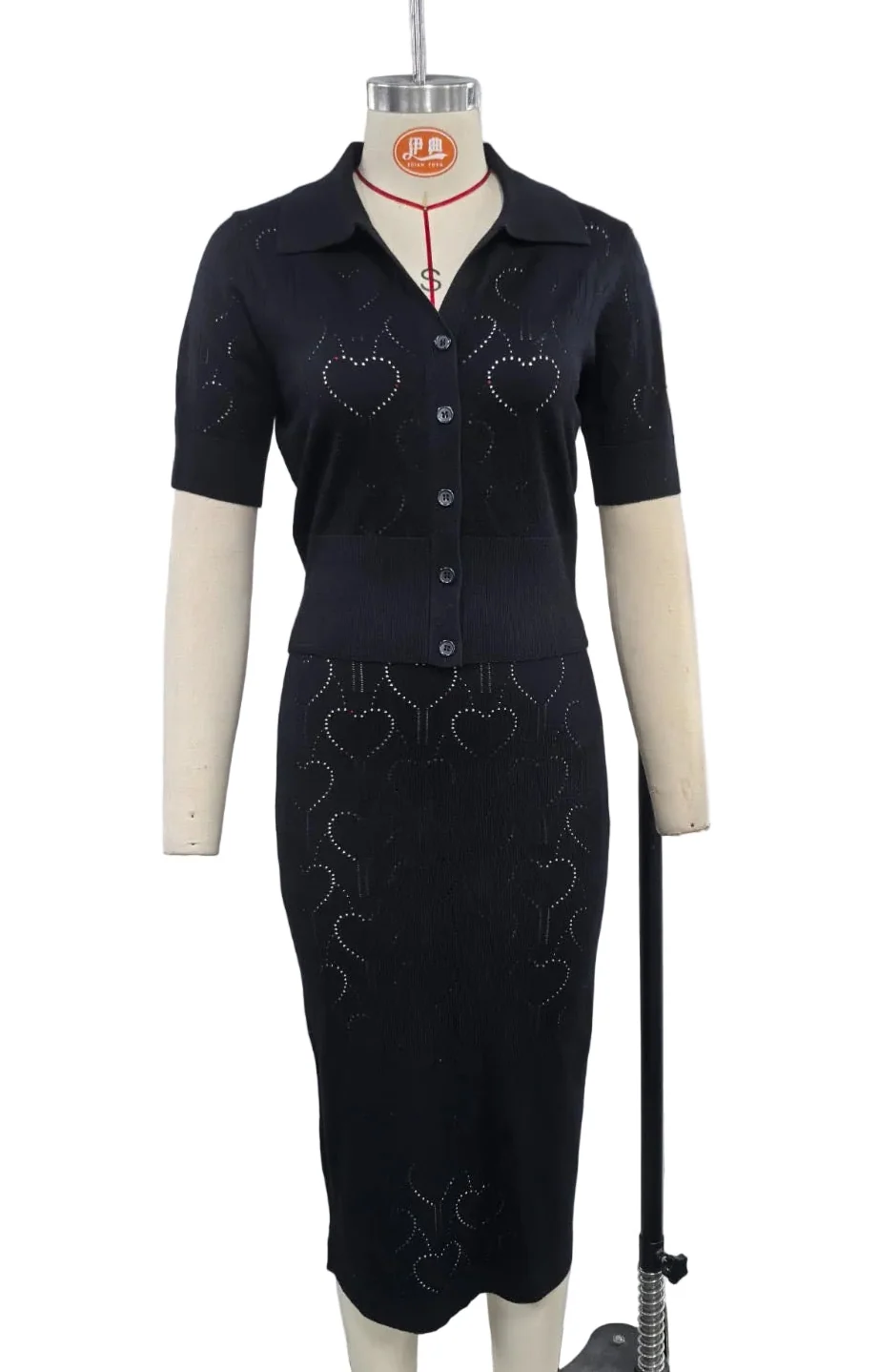 A two-piece women's knit set consisting of a short-sleeve button-front collared top and a matching knee-length skirt, displayed on a cream dress form. The dark navy knit fabric features embroidered heart motifs and is shown against a plain white background.
