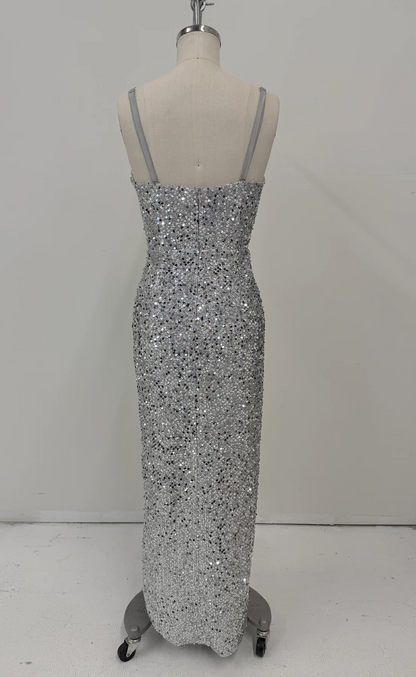 A floor-length silver sequined gown displayed on a dress form mannequin against a plain light gray studio wall and floor.