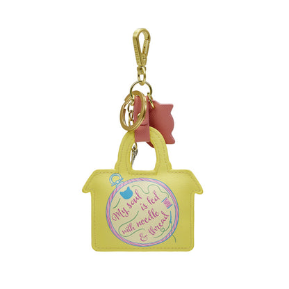 Yellow handbag-shaped keychain with pink bow and text on a white background