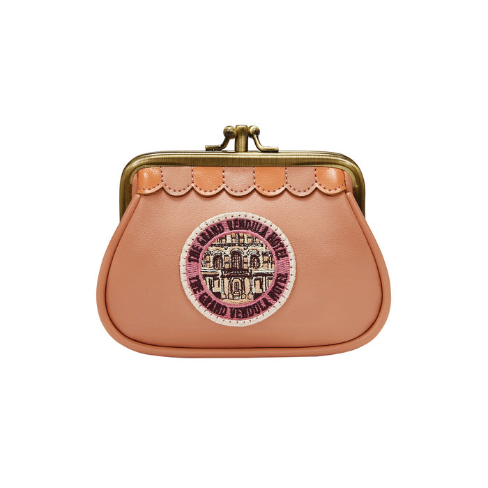 Small peach-colored purse with a decorative emblem on a white background