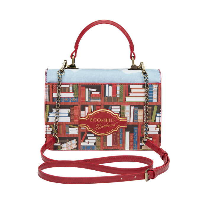Handbag with book-themed design and red handle on a white background