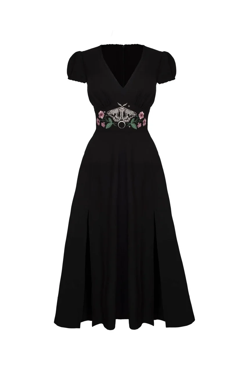 A black midi-length dress with short puff sleeves, a V-neckline, and a decorative embroidered waistband featuring a silver-tone circular brooch and pink floral accents, shown against a plain white background.