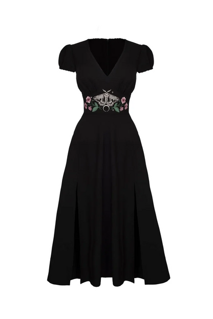 A black midi-length dress with short puff sleeves, a V-neckline, and a decorative embroidered waistband featuring a silver-tone circular brooch and pink floral accents, shown against a plain white background.