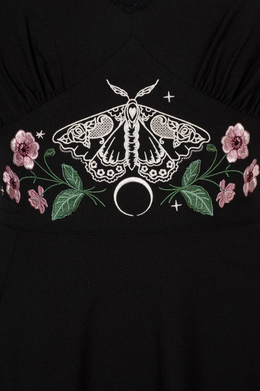 Black dress featuring a white embroidered moth and silver crescent moon motif, flanked by pink flowers and green leaves.