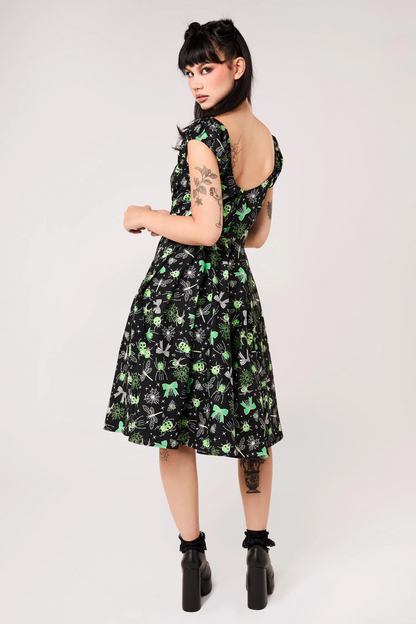 A woman modeling a black sleeveless fit-and-flare dress with a green and white floral print, shown from the back against a light gray studio background.