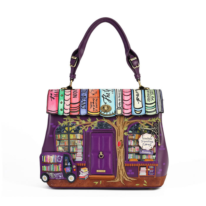 A purple handbag designed to look like a whimsical bookshop, featuring a purple handle, a purple door, bookshelves, and colorful book spines across the top flap, shown on a plain white background.