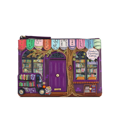 A purple zip-around clutch purse featuring a whimsical library storefront design with a purple door, bookshelves, a tree trunk, colorful book spines, and a small purple book truck, shown on a plain white background.