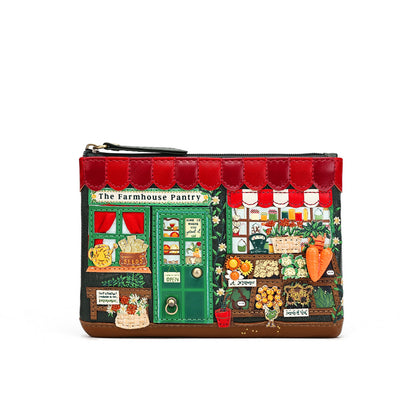 A small zip pouch designed to look like a detailed storefront illustration labeled 'The Farmhouse Pantry,' with red awnings, a green door, and illustrated produce and shop details, shown on a plain white background.