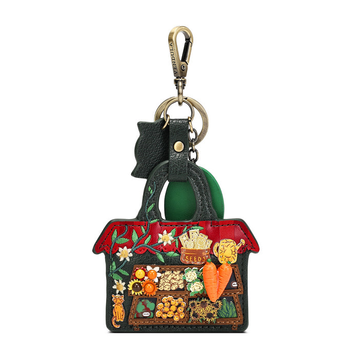 A Gucci handbag-shaped keychain or bag charm with a green leather handle, gold-tone clasp, and a detailed multicolor embroidered and embellished front panel featuring a market scene with fruits, vegetables, flowers, and a cat.
