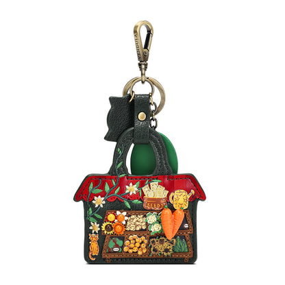 A Gucci handbag-shaped keychain or bag charm with a green leather handle, gold-tone clasp, and a detailed multicolor embroidered and embellished front panel featuring a market scene with fruits, vegetables, flowers, and a cat.