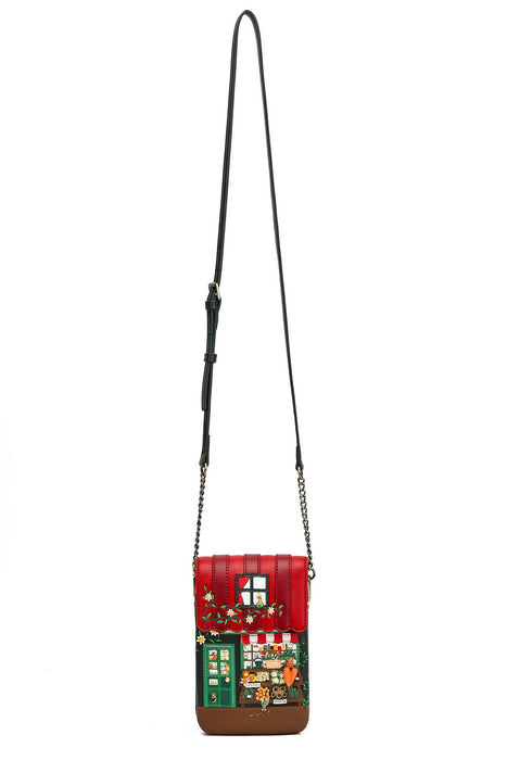 A small crossbody bag with a long black strap, featuring a red and green holiday storefront design with embroidered details, shown against a plain white background.