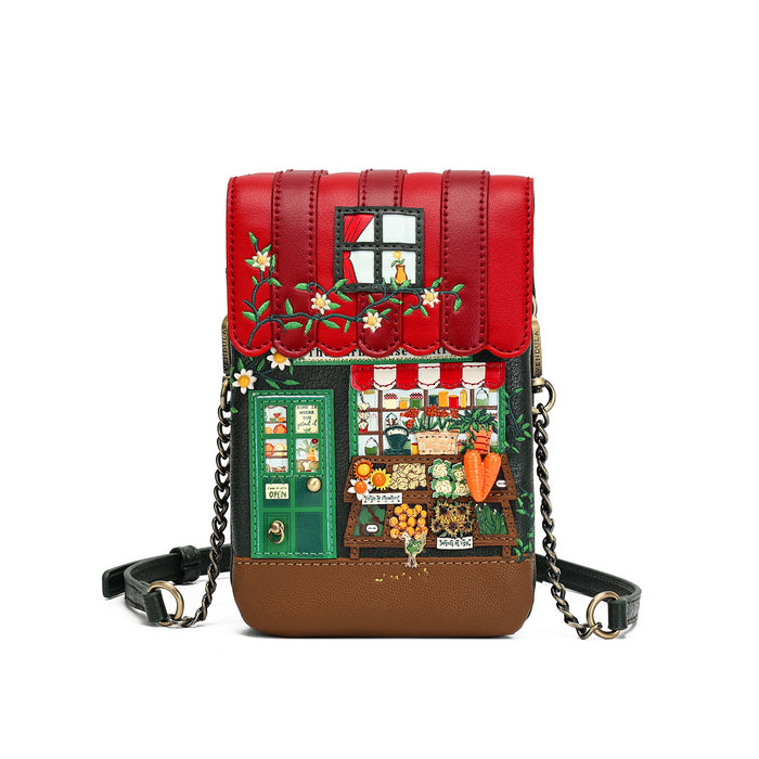 A small crossbody bag designed like a whimsical garden market shop facade, featuring a red upper facade with embroidered flowers, a green door, and a detailed market window scene, finished with a brown base and a black chain strap.