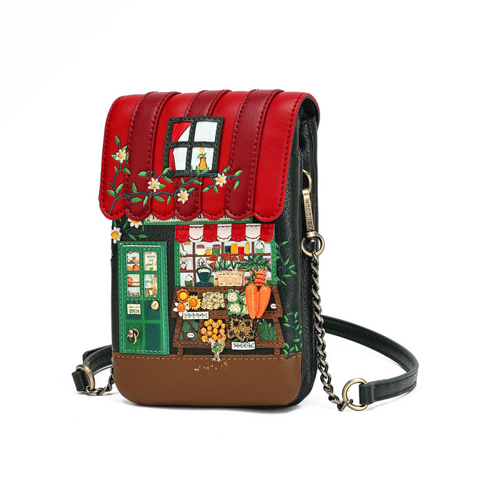 A small crossbody bag with a detailed, colorful illustration of a market stall on the front flap. The bag features a red faux-leather awning with embroidered flowers, a green door, a detailed shop window scene, and a brown base, complete with a black leather strap and a gold-tone chain link.