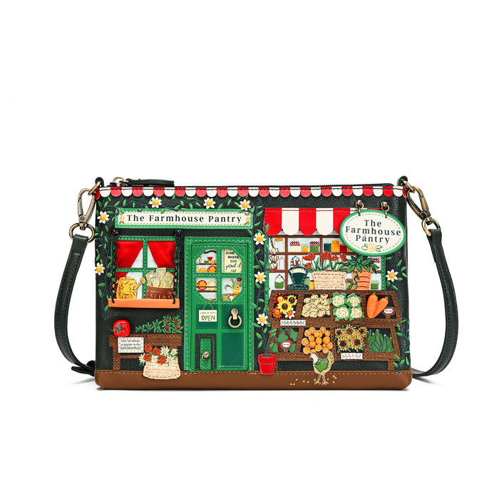 A rectangular shoulder bag designed to look like a whimsical 'The Farmhouse Pantry' storefront, featuring a green door, red-and-white striped awning, and detailed cartoon illustrations of vegetables, flowers, and market items. It has a black leather strap and gold-tone hardware, shown against a plain white background.