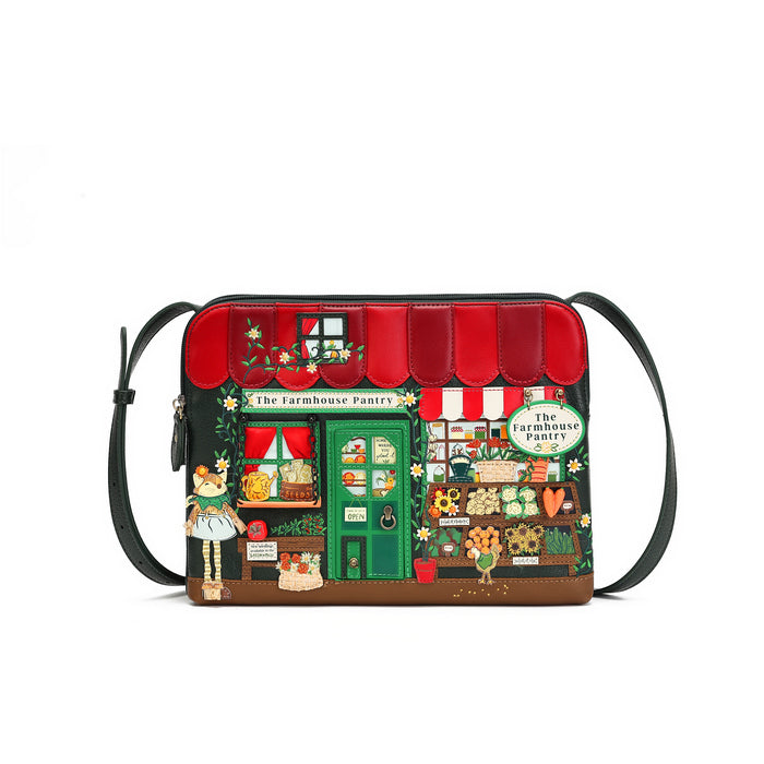 A small shoulder bag with a colorful printed design of a vintage-style bakery storefront labeled 'The Farmhouse Pantry.' The bag has a black strap, black trim, a red awning, green door and window details, and illustrated produce, flowers, and characters on the front.