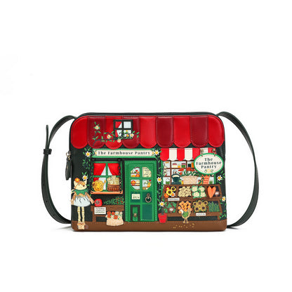 A small shoulder bag with a colorful printed design of a vintage-style bakery storefront labeled 'The Farmhouse Pantry.' The bag has a black strap, black trim, a red awning, green door and window details, and illustrated produce, flowers, and characters on the front.