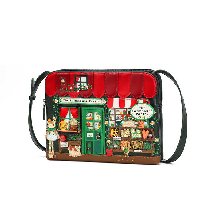 A black leather crossbody bag featuring an intricate, colorful embroidered illustration of 'The Farmhouse Pantry' storefront, complete with a red awning, green door, and various floral and vegetable details, shown on a plain white background.