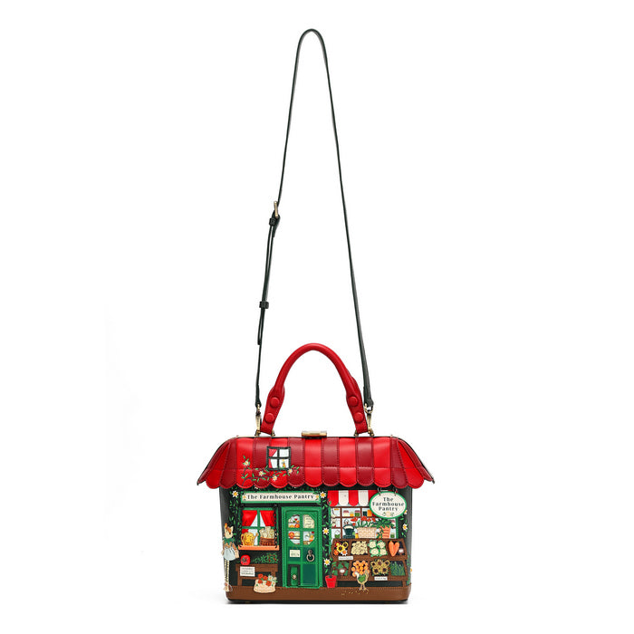 A house-shaped shoulder bag with a red roof and handles, featuring a detailed green storefront front with cartoon characters and a black shoulder strap, shown on a plain white background.