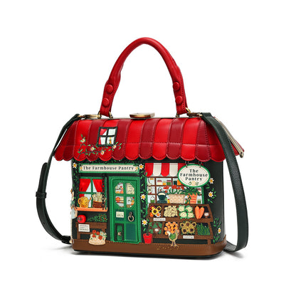 A structured handbag designed to look like a whimsical 'The Farmhouse Parlor' storefront, featuring a bright red faux-leather top handle and scalloped roof, with a detailed multicolor facade depicting a shop front, green door, and small decorative figures, shown on a white background.