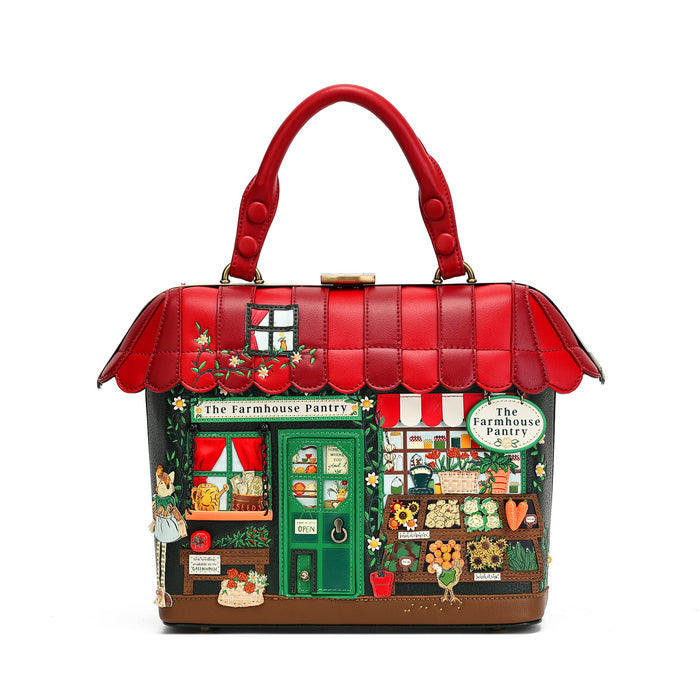 A structured red handbag shaped like a whimsical storefront, with a red top handle, scalloped red roof, and an illustrated front facade reading 'The Farmhouse Pantry' in green, cream, and red. The bag is photographed on a clean white background.