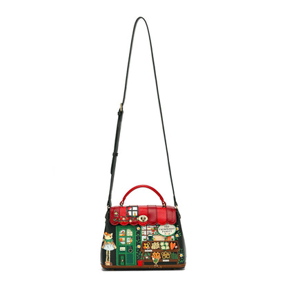 A Gucci handbag with a black leather body, a red top handle and trim, and a highly detailed, colorful patchwork illustration depicting a village scene with a green door, a white cat, and a speech bubble reading 'Nonna Maria'.