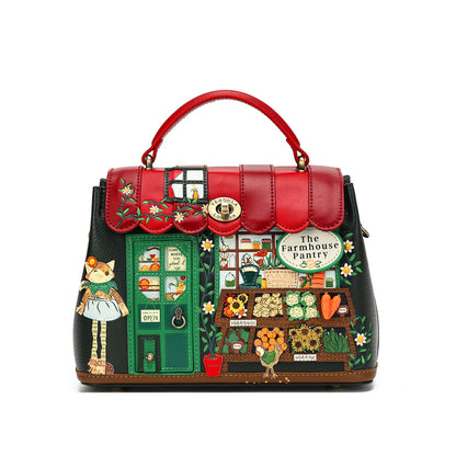 A structured handbag with a red top handle and a black body, decorated with a whimsical 'The Farmhouse Pantry' illustration featuring a cat, flowers, and produce.