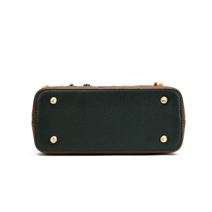 The bottom view of a dark forest green pebbled leather clutch or wallet-style handbag, featuring four brass rivets on the bottom corners and a decorative multicolor embroidered trim along the top edge.