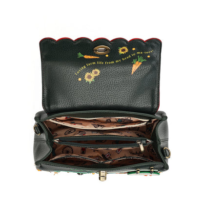 An open black pebbled leather handbag with a scalloped top edge, featuring embroidered carrots, sunflowers, and the phrase 'living farm life from my head to my toes' on the inside lid. The interior is lined with a brown patterned fabric and has multiple compartments.
