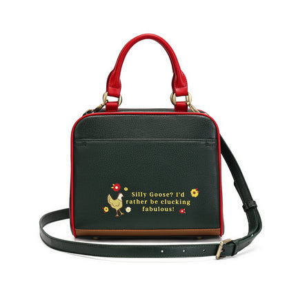 A structured black pebbled leather handbag with red leather handles and trim, featuring a brown leather base trim and a black shoulder strap. The front has a yellow embroidered chicken and the text 'Silly Goose? I'd rather be clucking fabulous!'.