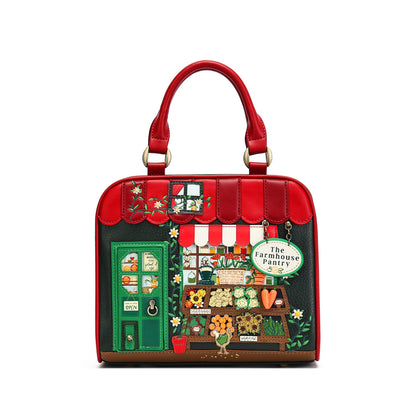 A red structured handbag with a whimsical embroidered 'The Farmhouse Pantry' market stall design on the front, featuring green handles and gold-tone hardware, set against a plain white background.