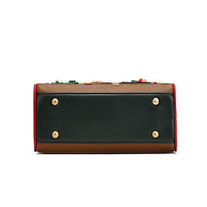 A rectangular leather clutch or wallet shown from the back, featuring a dark green pebbled leather back panel with four gold-tone rivets, a tan leather top and bottom, a red side border, and colorful decorative embellishments along the top edge.