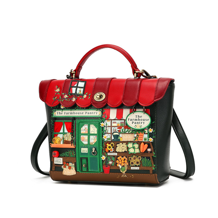 A structured handbag with a red top handle and red scalloped flap, featuring a detailed embroidered patch depicting 'The Farmhouse Pantry' storefront on the front. The bag has black sides, a brown base, and a green door in the embroidery, with a gold turn-lock closure on the flap.