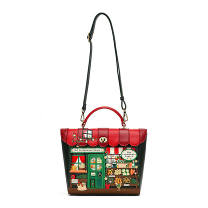 A structured handbag designed to look like 'The Freshhouse Bakery' from The Freshhouse Mystery Shop, featuring a red and black exterior with a detailed bakery storefront illustration on the front, complete with a green door, red awning, and colorful window displays. It has a top handle, a long shoulder strap, and gold-tone hardware.