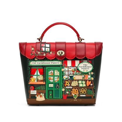 A structured handbag with a red top handle and a front panel printed with a whimsical farm market scene under a red awning, reading 'The Farmhouse Pantry.' The bag has red leather trim, a gold-tone oval clasp, and dark side panels, photographed on a plain white background.