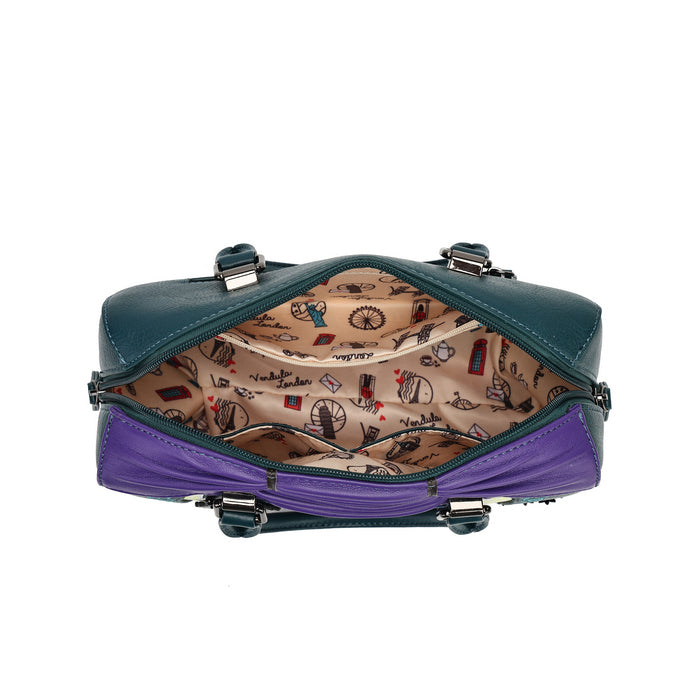 A small structured handbag shown open from the front, with a dark teal exterior, a purple lower section, silver-tone hardware, and a beige patterned interior printed with small illustrated motifs.