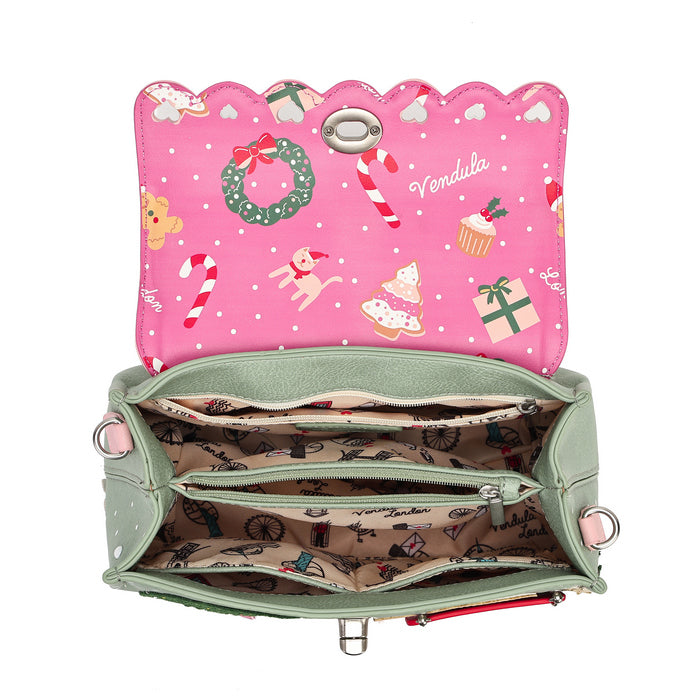 An open sage green handbag shown from the inside, featuring a bright pink interior flap decorated with Christmas motifs like candy canes, a wreath, and cupcakes, and a patterned beige lining with small printed illustrations.